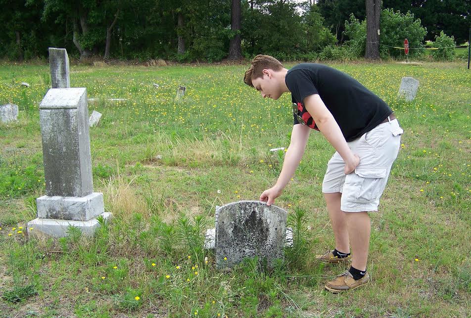 Boy Scout Isaac Wells examines a headstone knocked from its base at an abandoned cemetery on US 301 in Selma. Wells will spend this summer restoring the 140 graves in the cemetery, which was heavily vandalized 10 to 20 years ago and has no regular upkeep. JoCoReport.com Photo